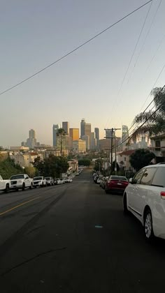 cars parked on the side of a road in front of a large cityscape