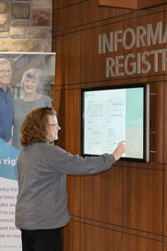 a woman standing in front of a sign pointing to information register on the side of a wall