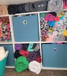 a closet filled with lots of different colored clothes and blankets on top of blue bins