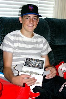 a young man sitting on a couch holding a box filled with baseball caps and other items