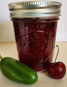 a pickle next to a jar of jam and a green pepper on a table