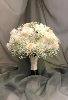 a bouquet of white roses and baby's breath sits on a gray satin background