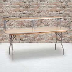 a wooden table sitting in front of a brick wall with two metal shelves on it