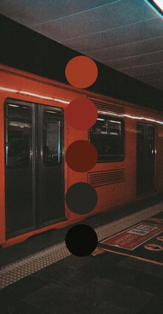 an orange train parked next to a loading platform with circles hanging from it's ceiling