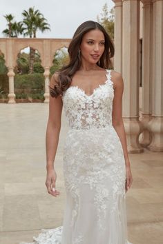 a woman in a white wedding dress standing on a stone walkway with palm trees behind her