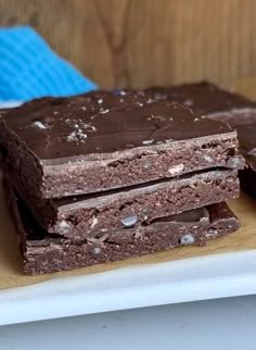 three pieces of chocolate brownie on a white plate next to a blue towel and wooden background