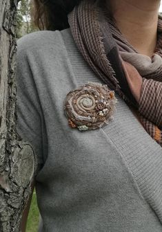 a woman standing next to a tree with a scarf around her neck and a flower brooch on it