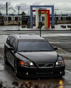 a black car parked in front of a gas station on a rainy day with no one around