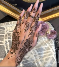 a woman's hand with henna tattoos on it and flowers in the background