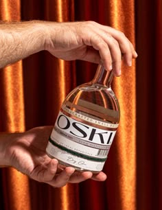 a hand holding a bottle of oski vodka in front of a curtained background