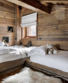 two beds in a room with wooden walls and white fur on the floor, one has a teddy bear