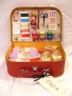 an open suitcase filled with lots of crafting supplies and thread on top of a white sheet