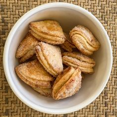 a white bowl filled with powdered sugar covered pastries on top of a woven table cloth