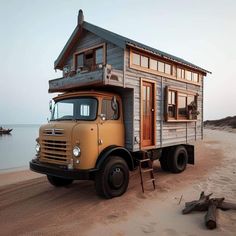 a yellow truck parked on top of a sandy beach next to the ocean with a tiny house on it's back