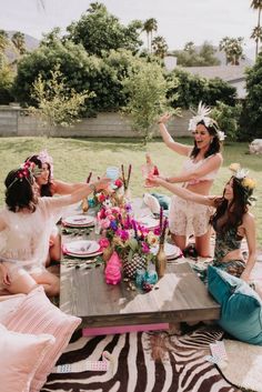 three women sitting at a picnic table with plates and cups in their hands, wearing flower crowns