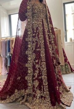 a woman in a red and gold bridal gown standing next to a rack with clothes on