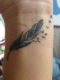 a small feather tattoo on the wrist with birds flying around it and stars in the sky