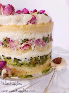 a multi layer cake with white frosting and pink flowers on top, sitting on a plate