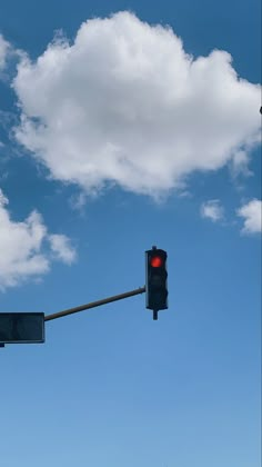 a traffic light hanging from the side of a metal pole under a cloudy blue sky