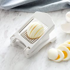 an egg slicer on a marble counter top with sliced eggs in the foreground