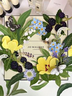 an arrangement of flowers and butterflies on display in front of a sign that says jo malone london