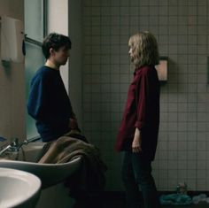 two people standing in a bathroom next to a sink