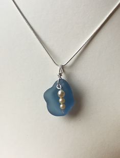 a blue sea glass necklace with two pearls hanging from it's end on a silver chain