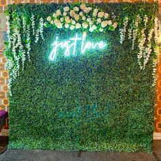 a green wall with white flowers and greenery on it that says, just live