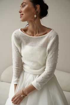 a woman in a white dress and pearls on her sweater is looking away from the camera