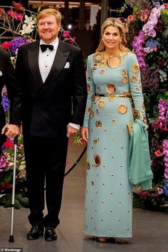 the man and woman are walking their dog down the hall together, dressed in black tuxedos