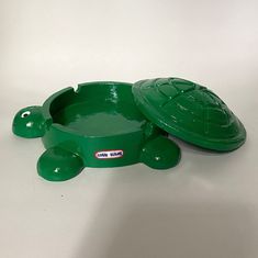 a green turtle shaped bowl sitting on top of a white table next to a toy turtle