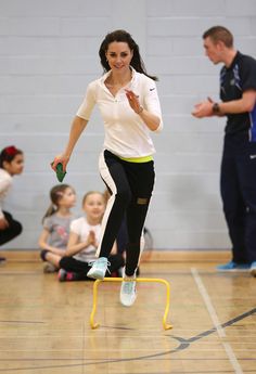 a woman in white shirt and black pants jumping over a small yellow object on top of a wooden floor