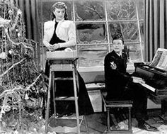 an old black and white photo of two people in front of a piano near a christmas tree