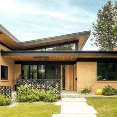 a modern home with wood siding and black iron railings on the front door, windows, and landscaping