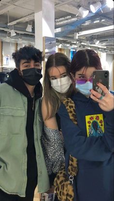 three people wearing face masks while looking at a cell phone and taking a selfie