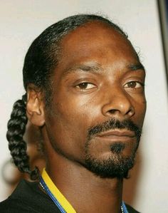 a man with braids on his hair looks off to the side while standing in front of a white wall