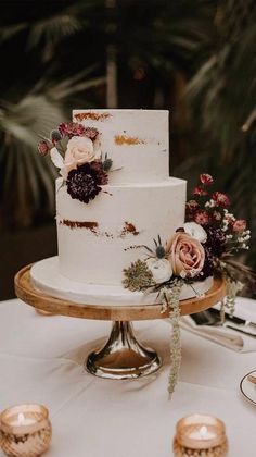 a white wedding cake with flowers and greenery on the top is sitting on a table