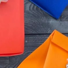 a person holding an orange piece of paper next to other colored papers on a wooden table