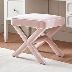 a pink stool sitting on top of a wooden floor next to a white dresser and mirror