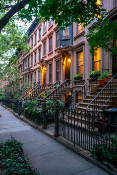 a row of brownstone townhouses with wrought iron railings and trees in the foreground