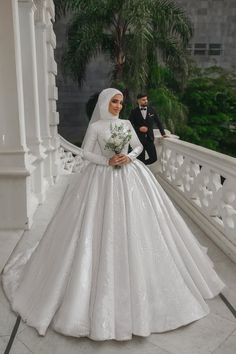 a woman in a white wedding dress standing on a balcony next to a man in a tuxedo