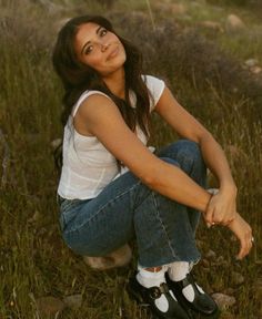 a young woman sitting in the grass with her hand on her knee and looking up