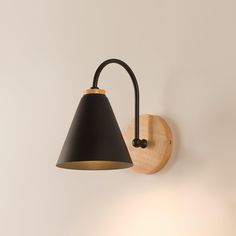 a wall light with a black shade hanging from it's side on a white wall