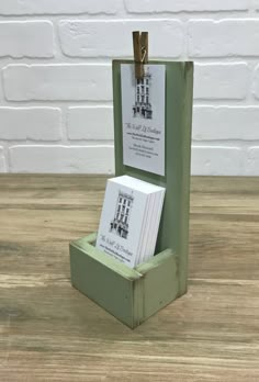 a small green box with some cards in it on a wooden table next to a white brick wall