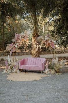 a pink couch sitting under a palm tree in front of a wedding sign with flowers