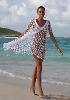 a woman standing on top of a beach next to the ocean wearing a white crocheted cover up