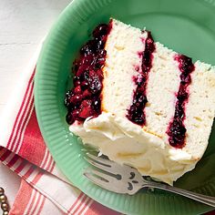 a piece of cake with white frosting and blue berries on top sits on a green plate