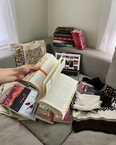 a person is reading a book on the couch next to some books and other items