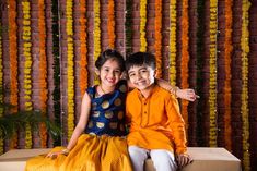 two children are sitting on a box in front of a backdrop of orange and yellow flowers