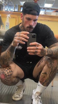 a man with tattoos is looking at his cell phone while sitting on the floor in front of him